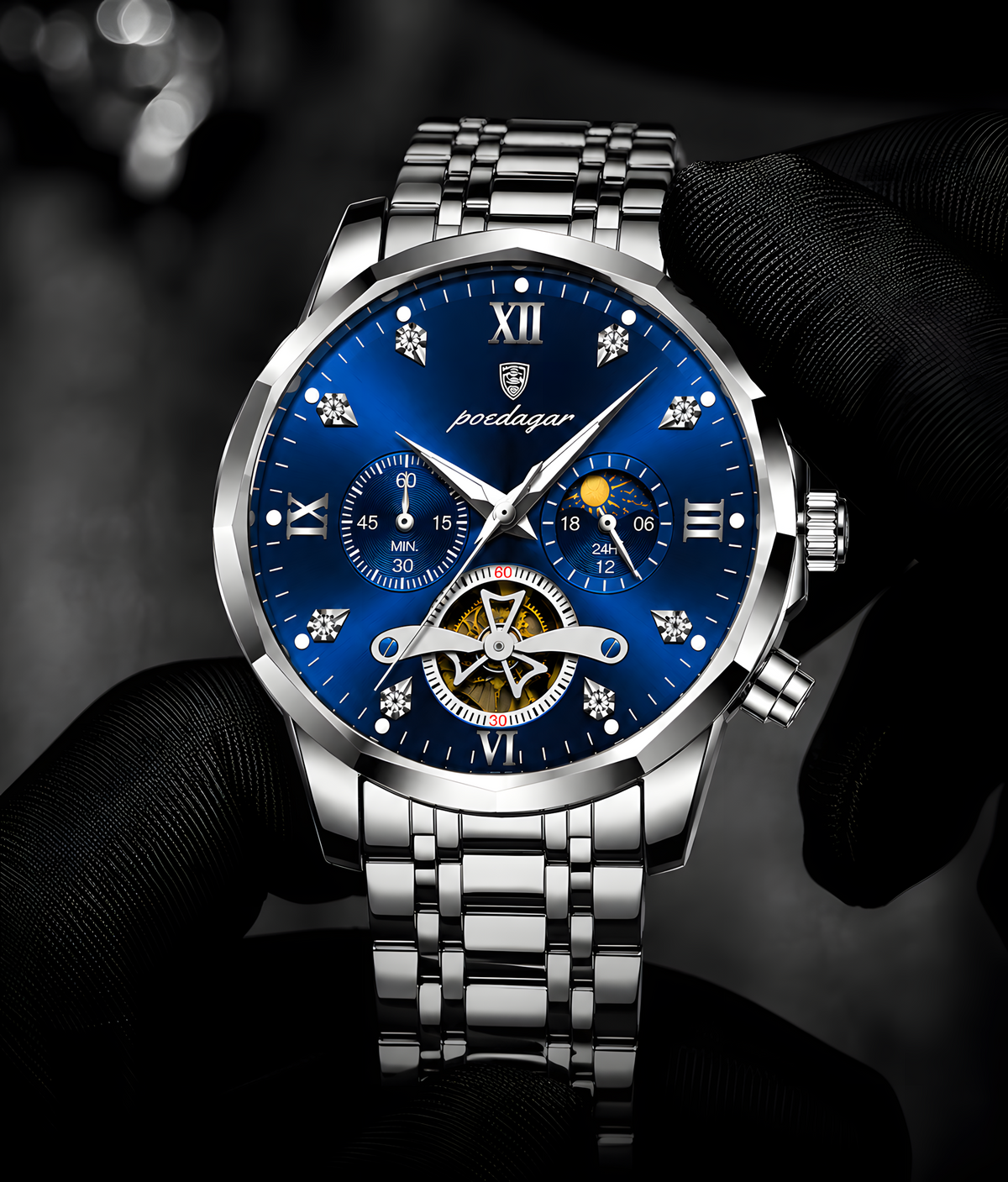 A close-up of a silver-tone metal wristwatch with a vivid blue dial, held by a hand wearing a black glove. The watch features Roman numeral hour markers, subdials, a moonphase indicator, and a visible gold-toned tourbillon cage at the bottom of the dial.