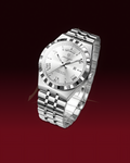 A silver-toned SatinCraft watch with a stainless steel link bracelet, featuring a silver dial, Roman numeral hour markers, and a fluted bezel, set against a dark red gradient background.